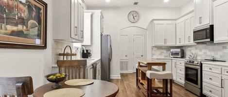 A modern kitchen with white cabinetry, a dining area with a wooden table and chairs, and a kitchen island.
