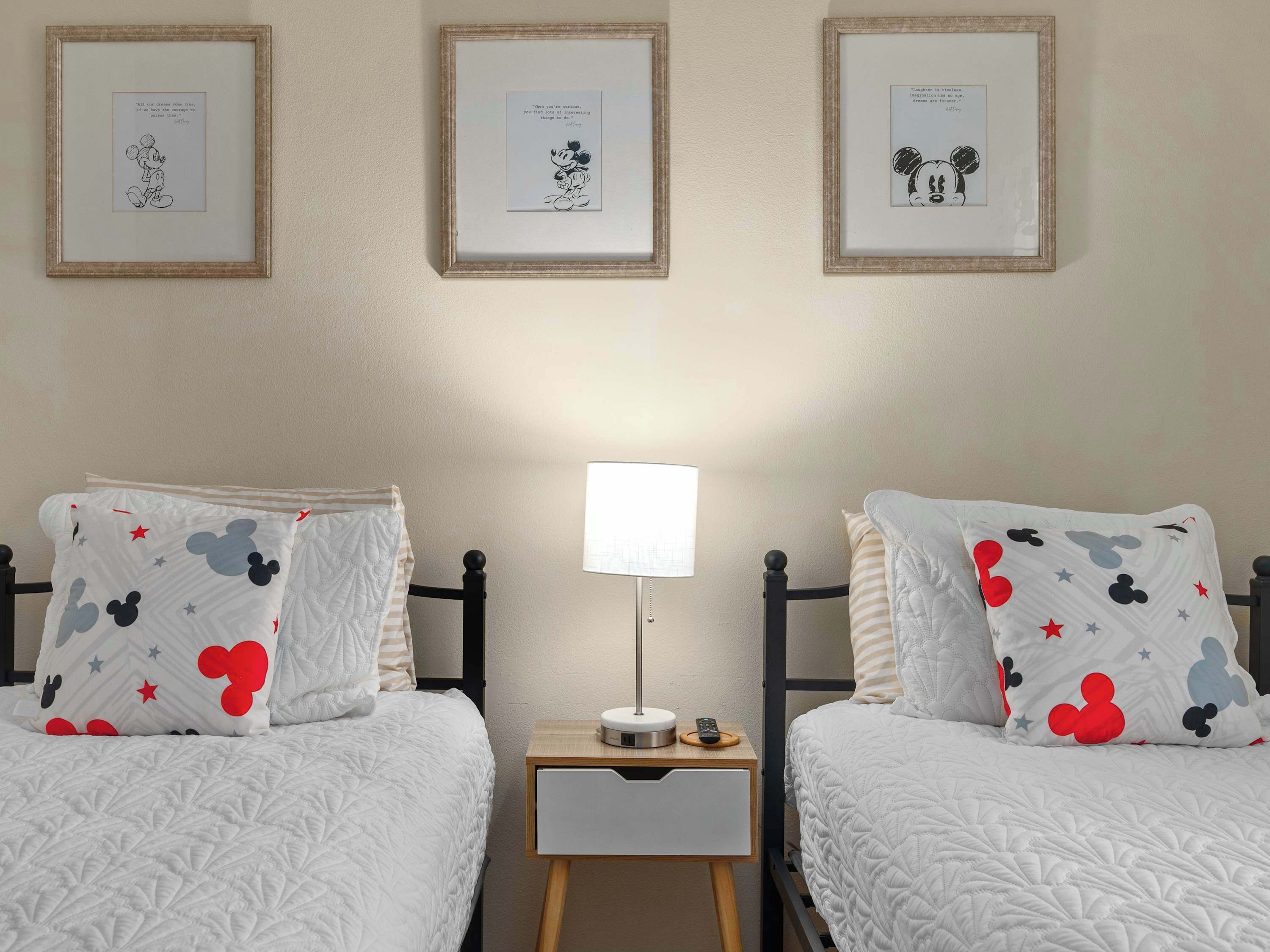 Une chambre d’hôtel avec deux lits, chacun agrémenté d’oreillers à l’effigie de Mickey Mouse, une table de chevet avec une lampe et des tableaux encadrés accrochés au mur.