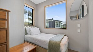 A bedroom with a bed, a window, a mirror, and a wooden bench. - Alpine Haven on Poole Lane (Queenstown)