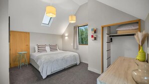Ein Schlafzimmer mit Bett, Nachttischen, einem Kleiderschrank, einem Oberlicht und einem fenster mit Vorhängen.