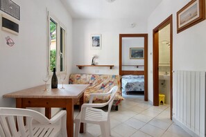 A compact room with a dining table, chairs, a sofa, a bed, and a small bathroom. - Two-room Apartment with Veranda and Garden 100m from the Sea - Villaggio Sole e Mare (Rio)