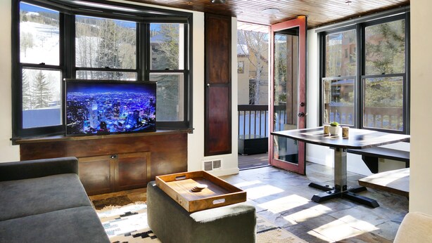 A room with a large window, a television, a table, and a sofa. - Ski-In Ski-Out Retreat in the Heart of Mtn Village (Telluride)