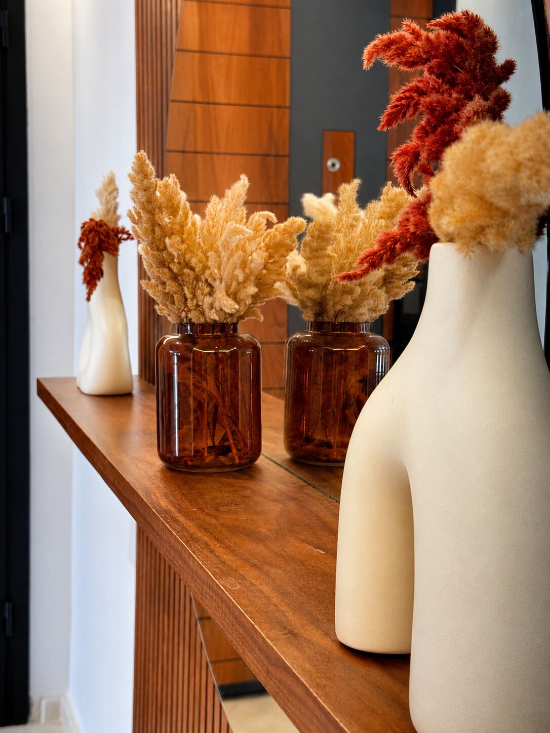 A wooden shelf with three vases containing dried plants.