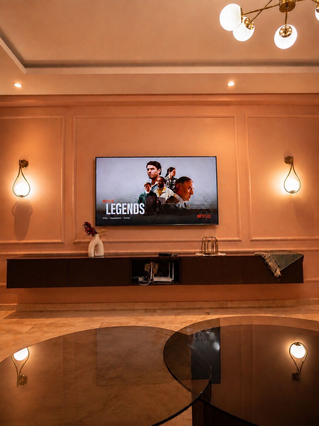 Un salon moderne doté d’un grand téléviseur à écran plat fixé au mur, d’une table basse en verre et d’appliques murales.