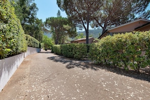 A paved driveway leading to a building with a white exterior and a red roof, surrounded by dense greenery and trees. - Two-room Apartment with Veranda and Garden 100m from the Sea - Villaggio Sole e Mare (Rio)