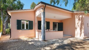 A single-story building with a flat roof, a covered patio area, and a gravel driveway. - Two-room Apartment with Veranda and Garden 100m from the Sea - Villaggio Sole e Mare (Rio)