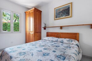 Ein Schlafzimmer mit einem Bett, einem Kleiderschrank, einem Gemälde und einem Fenster mit Blick auf Grünflächen.