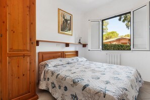 Ein Schlafzimmer mit einem hölzernen Bett, einem Bild an der Wand und einem Fenster mit Blick ins Grüne.