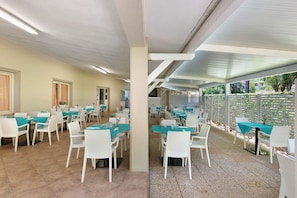 A restaurant with multiple tables and chairs, a tiled floor, and a ceiling with fluorescent lighting. - Three-Room Apartment with Garden 100 Meters from the Beach - Sole e Mare Tourist Village (Rio)