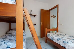 A room with two wooden bunk beds, a door with a geometric mirror, and a small shelf with a light fixture. - Three-Room Apartment with Garden 100 Meters from the Beach - Sole e Mare Tourist Village (Rio)