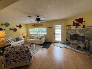 A living room with a fireplace, a ceiling fan, and a couch with decorative pillows. - C & J’s Old Sassa Cottage - Old Homosassa Waterfront Retreat - Private Dock (Homosassa)