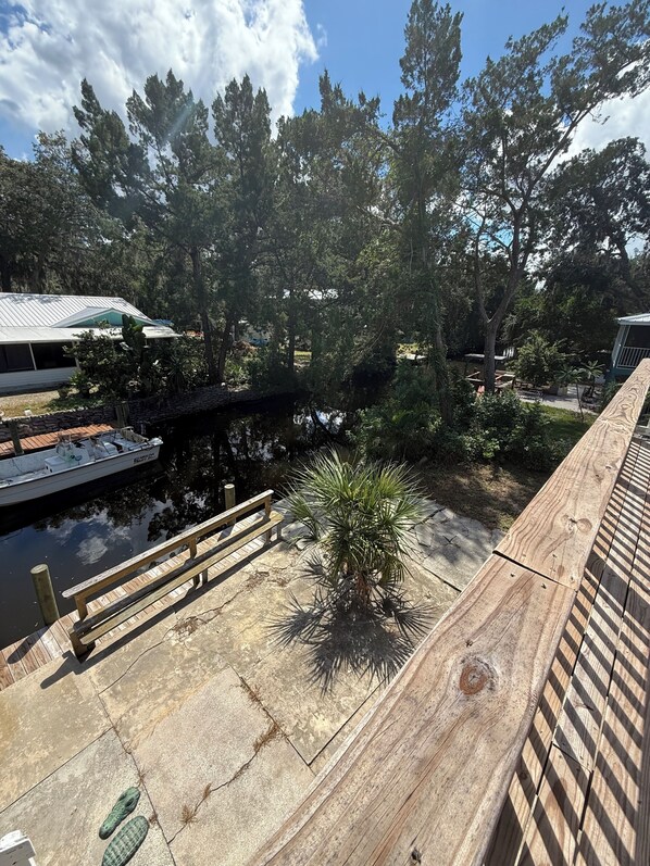 A wooden deck with a small palm tree, a dock with a boat, and a stone pathway.