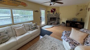 Una sala de estar con un sofá color beige, un sofá estampado con motivos florales, una chimenea y un ventilador de techo.