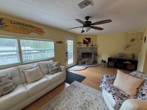 A living room with a beige sofa, a floral-patterned sofa, a fireplace, and a ceiling fan.