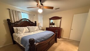 Un dormitorio con cama de madera, ventilador de techo, cómoda y espejo.