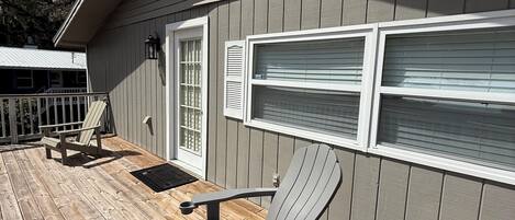 A wooden deck with Adirondack chairs and a covered patio area adjacent to a building with a window and a door.