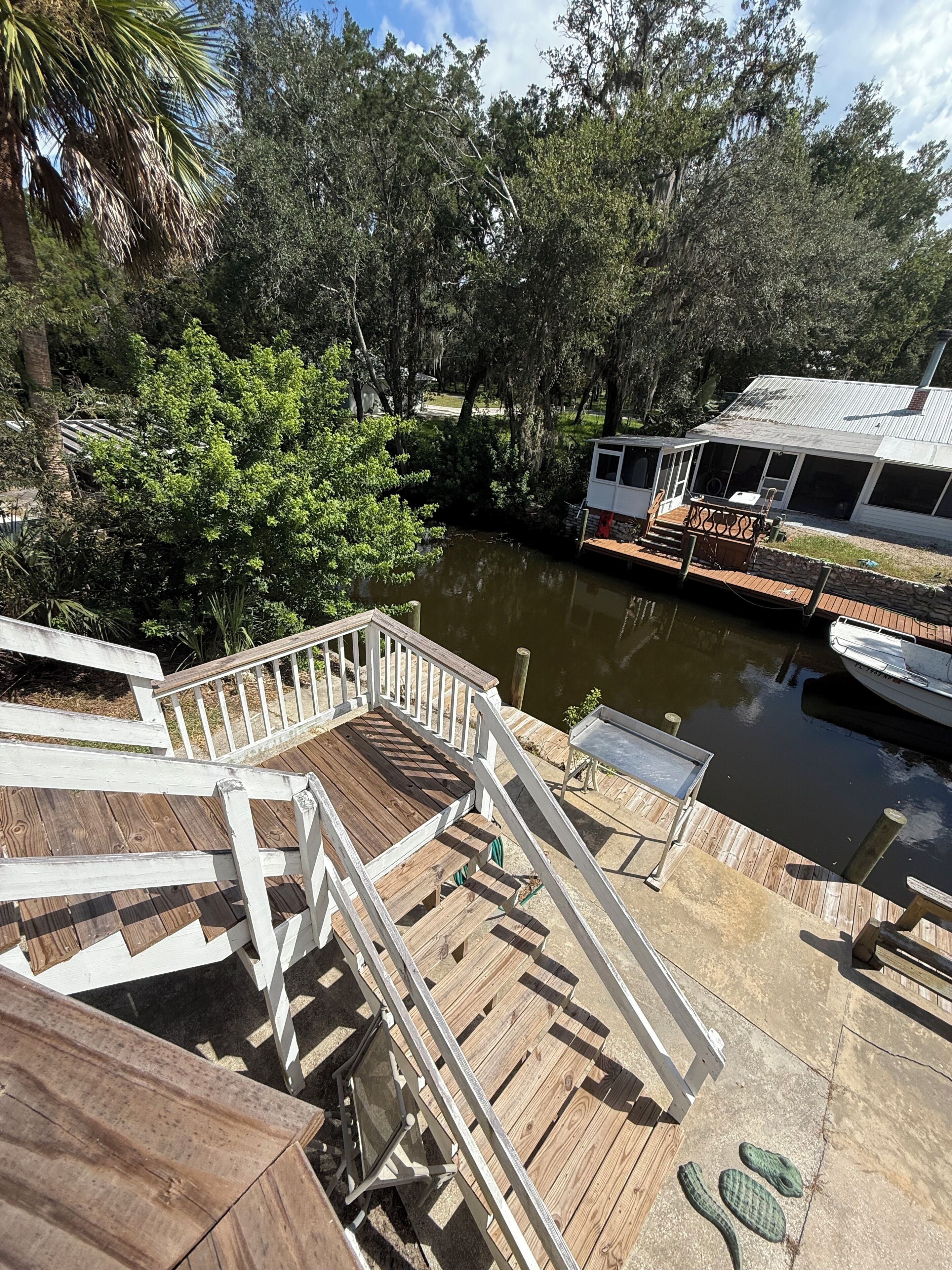 A wooden deck with a railing, a dock extending into a body of water, and a boat docked on the right.