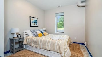 A bedroom with a bed, a nightstand, a lamp, a framed picture, and a window.