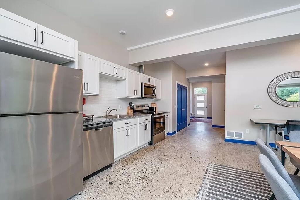 Una cocina moderna con electrodomésticos de acero inoxidable, armarios blancos y piso con textura.