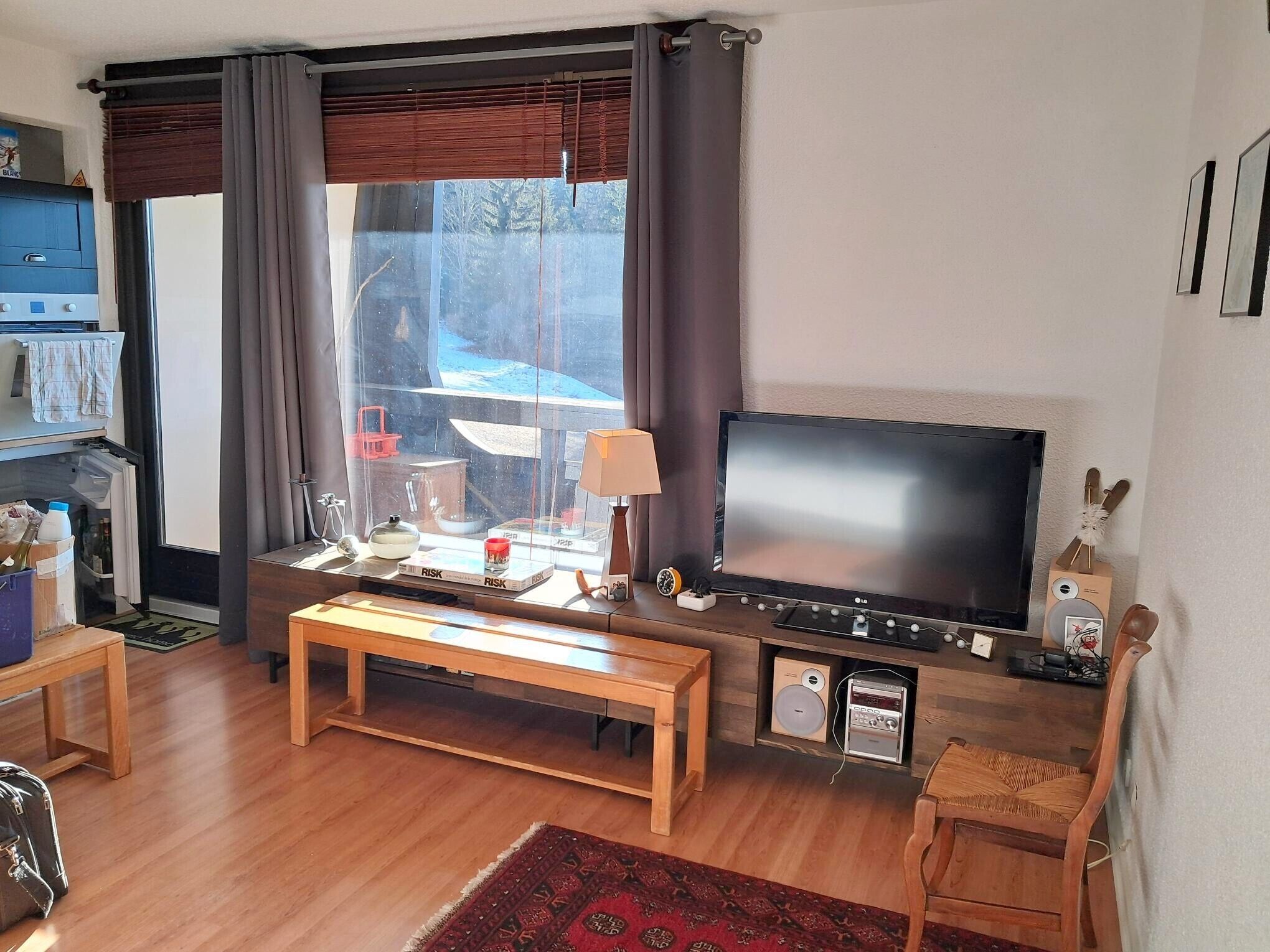 Una sala de estar con televisión de pantalla plana, muebles de madera, una mesita y un banco.