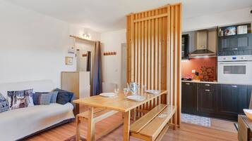 Een gezellige, compacte ruimte met een kitchenette, een eethoek met een houten tafel en bank, en een bank met gestreepte kussens.