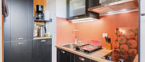 Une cuisine moderne avec des meubles de couleur sombre, une hotte en acier inoxydable et un dosseret carrelé.