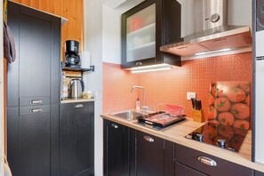 Een moderne keuken met donkere kastjes, een roestvrijstalen afzuigkap en een betegelde achterwand.