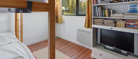 A room with a bunk bed, a bookshelf with books and toys, a television, and a window with a view of trees and mountains.
