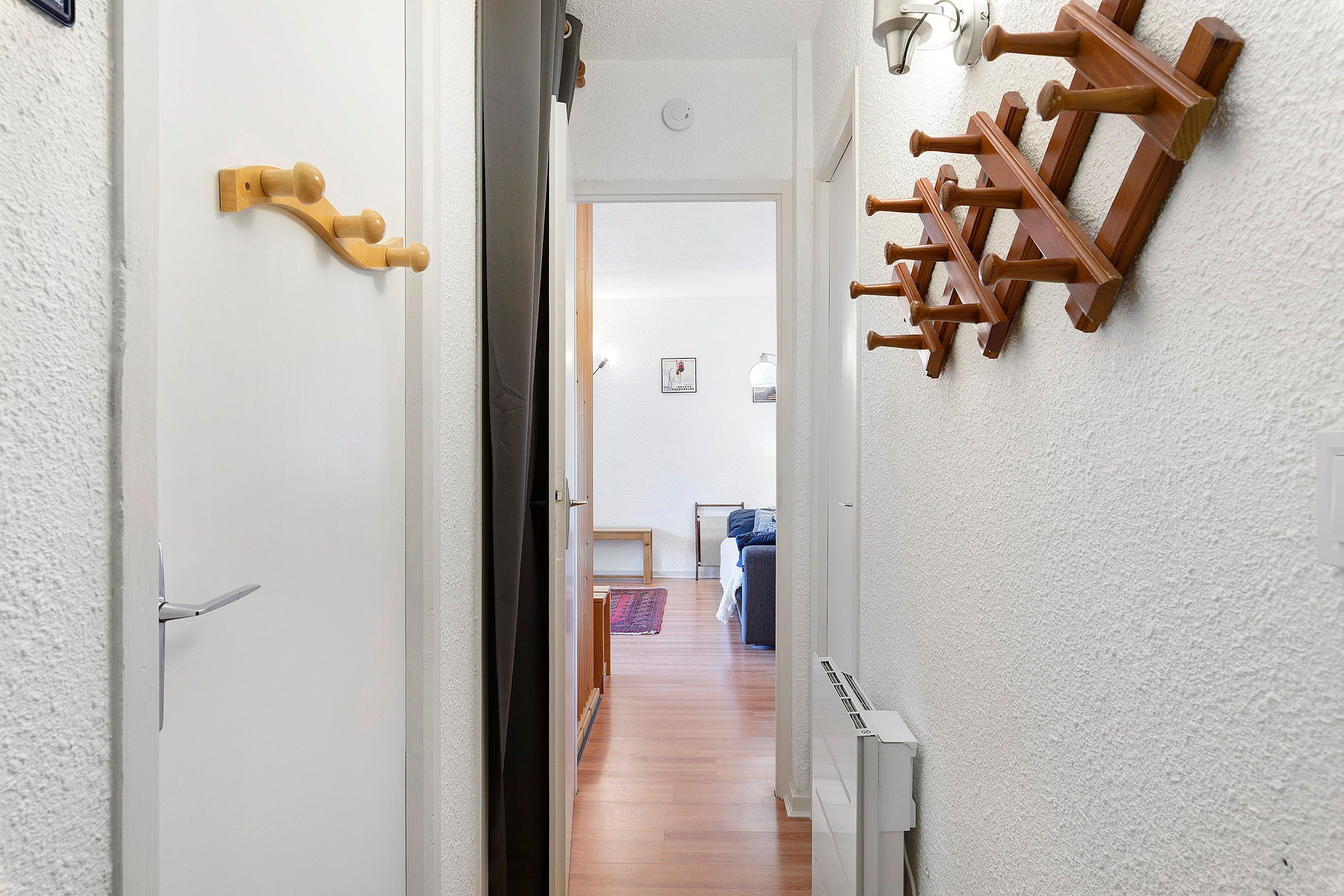 Un corridoio con una porta bianca, un termosifone e una rastrelliera in legno con ganci.