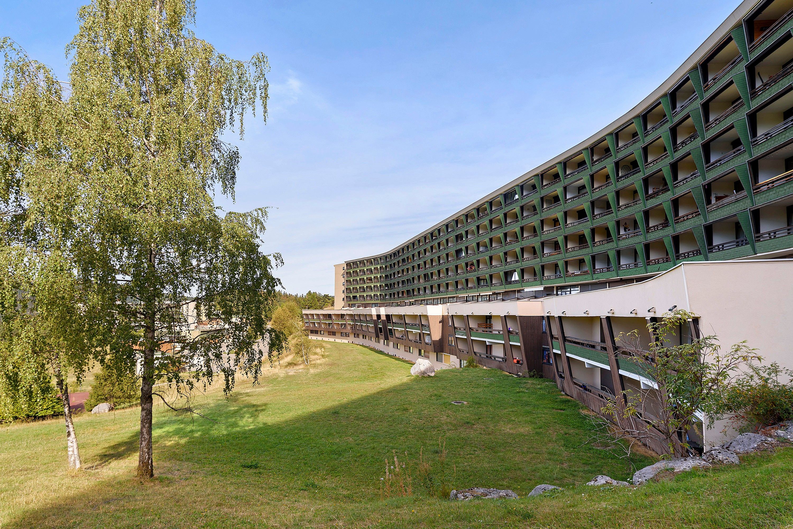 A multi-story building with a curved facade, outdoor seating area, and a tree in the foreground.