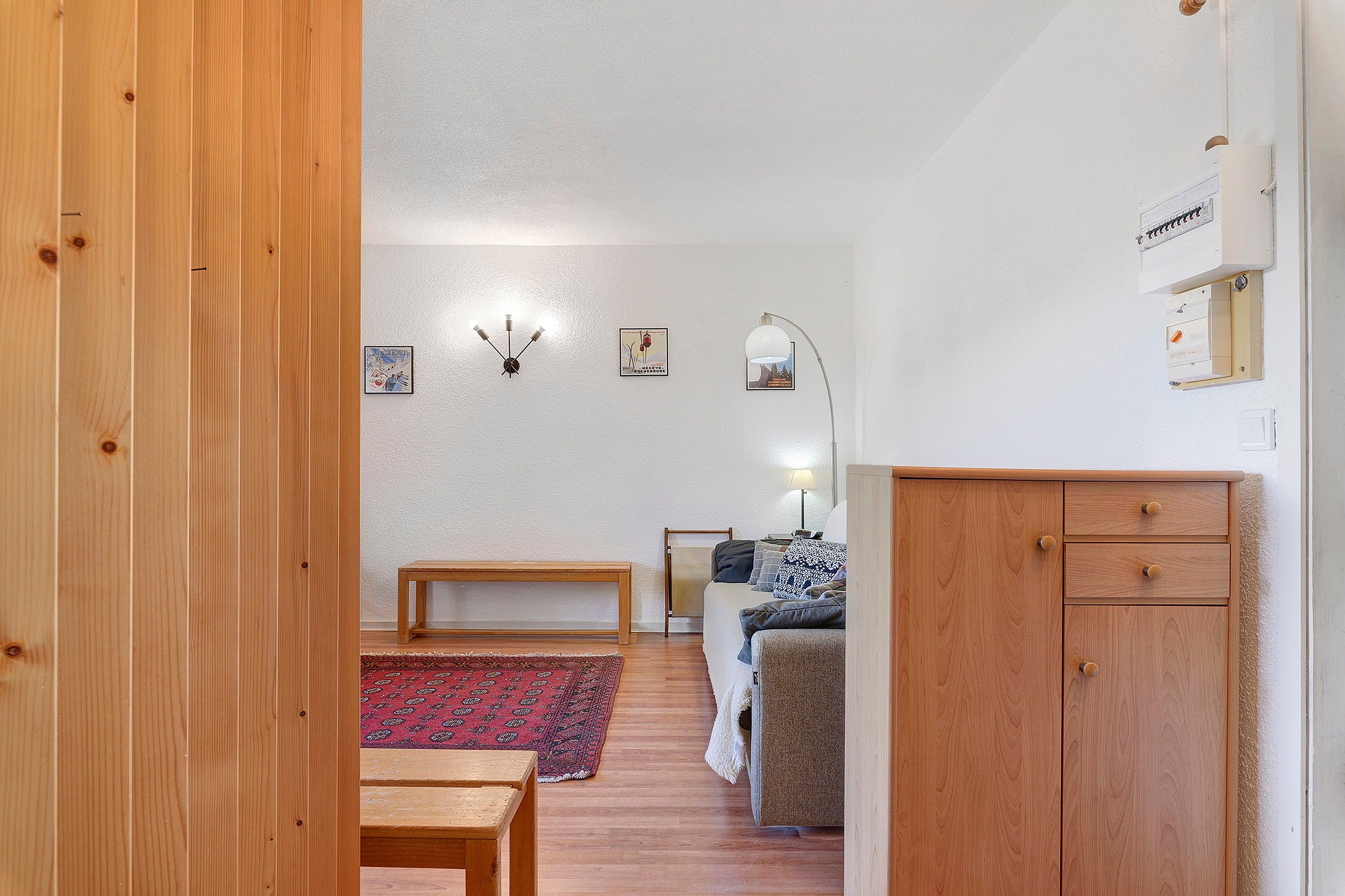 Een kamer met houten vloer, een bankje, een bank, een kleine tafel, een lamp en een kast.