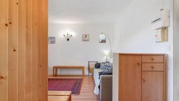 Een kamer met houten vloer, een bankje, een bank, een kleine tafel, een lamp en een kast.