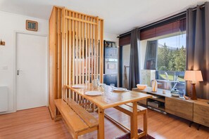 A dining area with a wooden table set for two, a bench, and a view of a mountain landscape through a window.