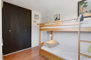 Een slaapkamer met een stapelbed met houten frame, een wit matras en een deur met een donker paneel.
