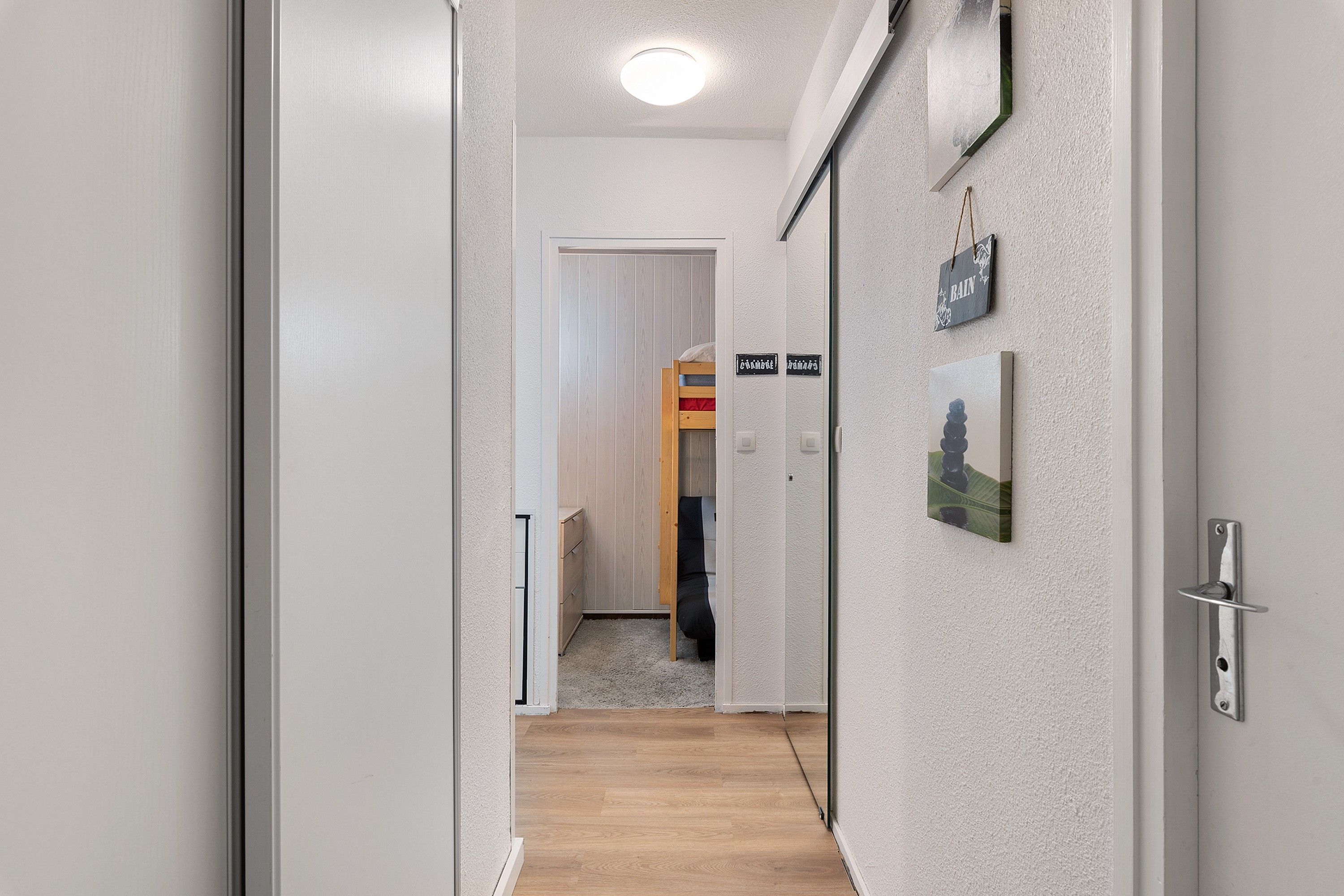 A hallway with a wooden floor, a door with a sign, and a wall-mounted picture.