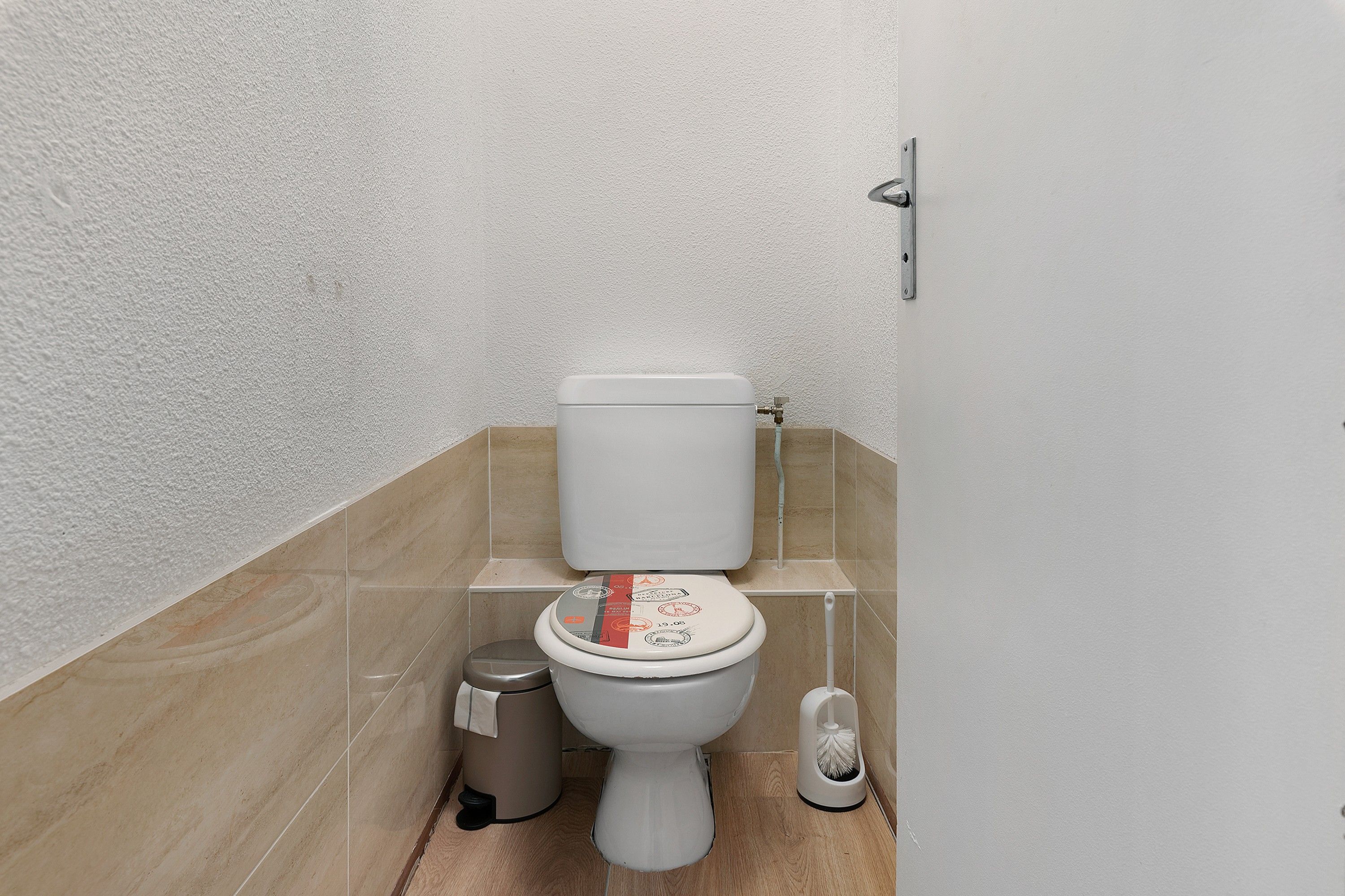 Een compacte badkamer met toilet, een prullenbak en een schoonmaakborstel.