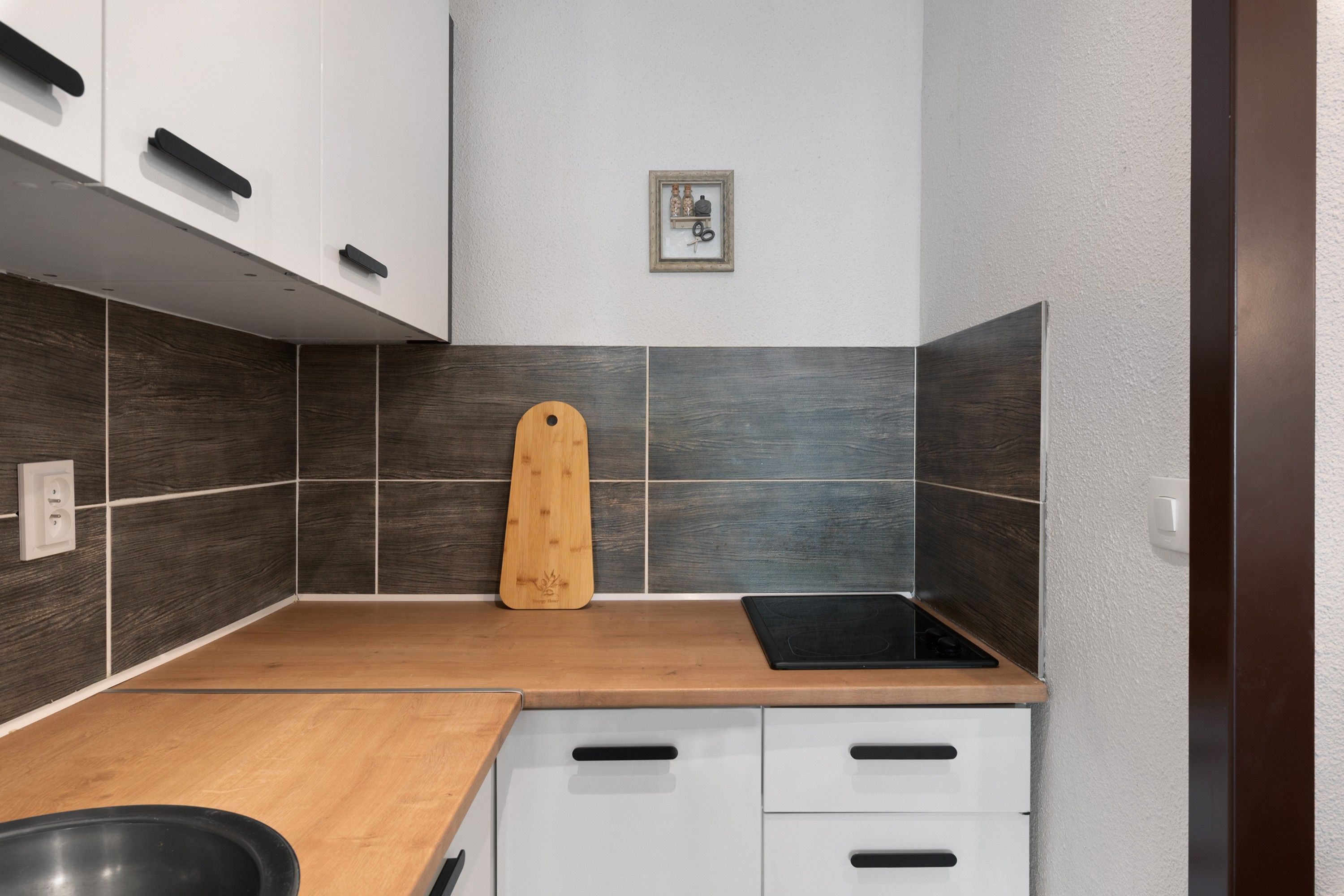Una cocina con encimera de madera, armarios blancos, un lavabo negro y un cuadro en la pared.