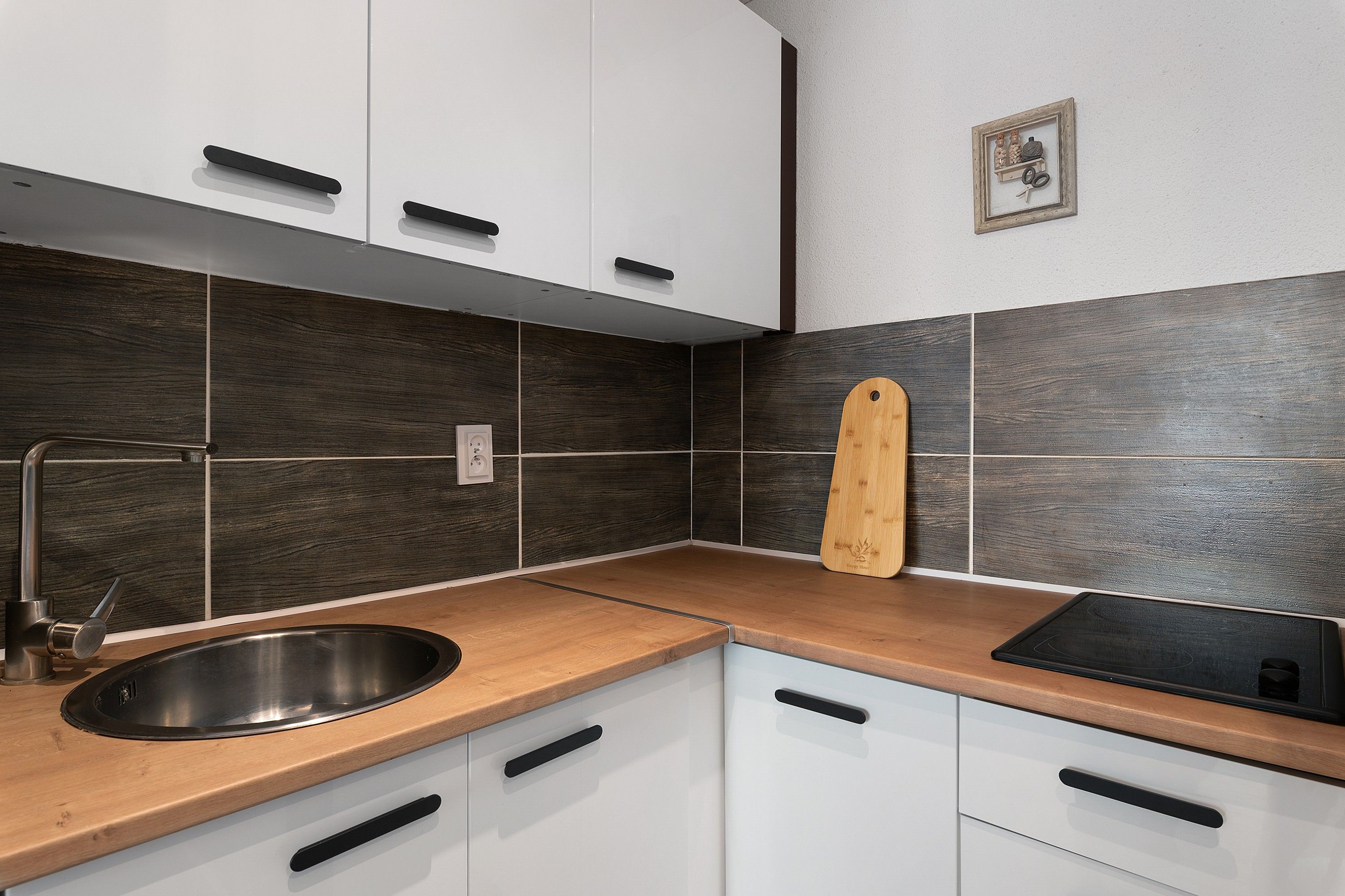 A modern kitchen with white cabinets, a wooden countertop, a stainless steel sink, and a black electric stove.