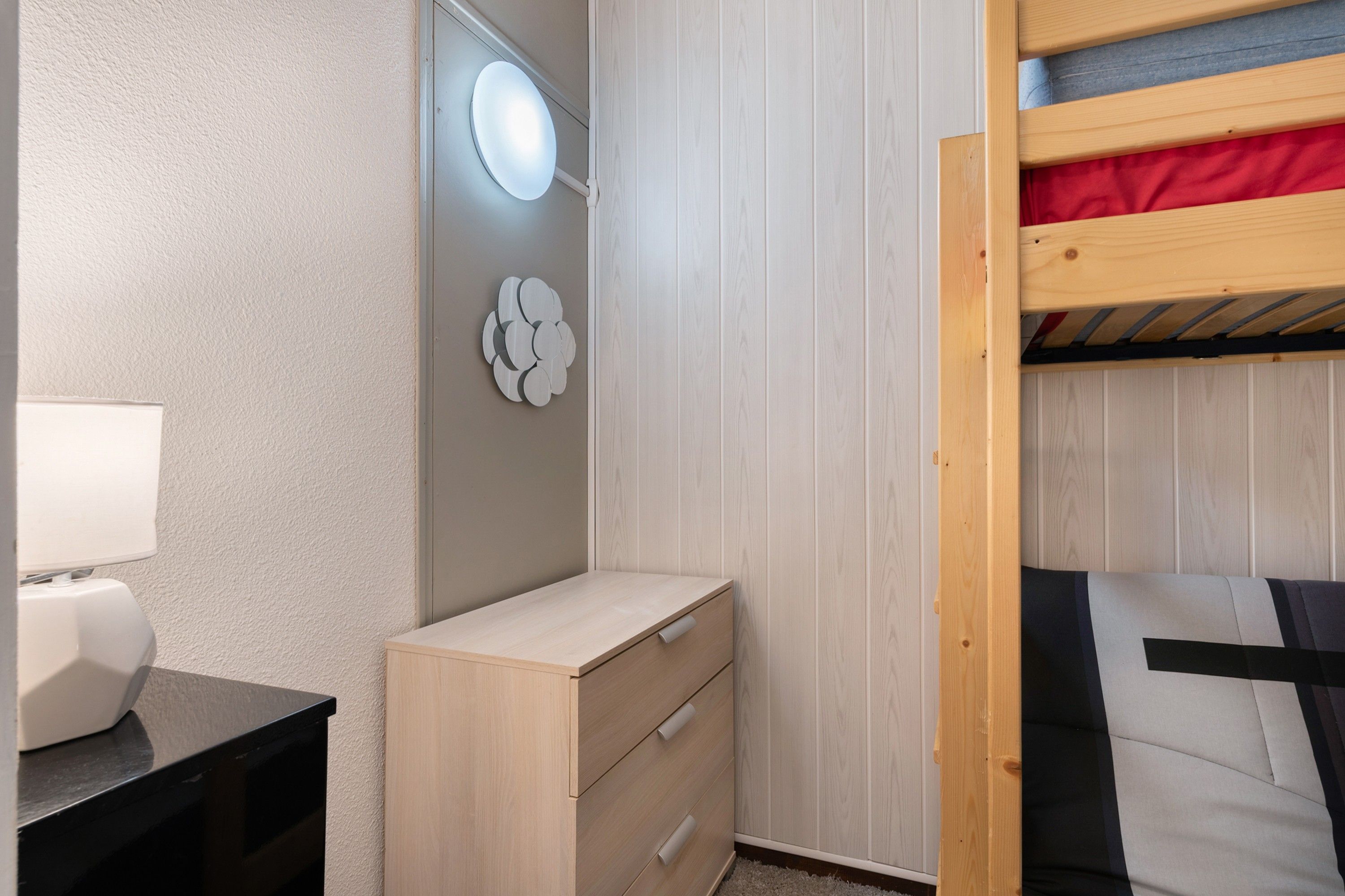 Un dormitorio con literas, una mesita de noche con lámpara, un aparador y un espejo montado en la pared.