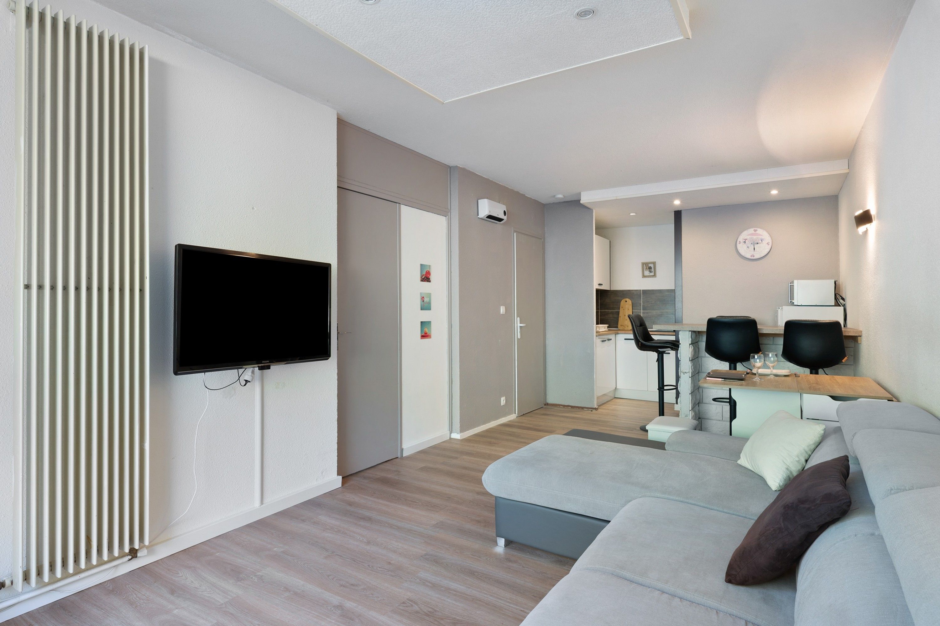 A modern living room with a flat-screen TV, a sofa, a coffee table, and a kitchen area in the background.