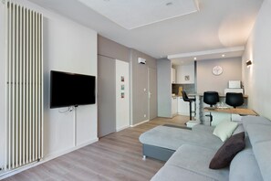 Ein modernes Wohnzimmer mit Flachbildfernseher, einer Couch, einem Couchtisch und einer Küchenzeile im Hintergrund.