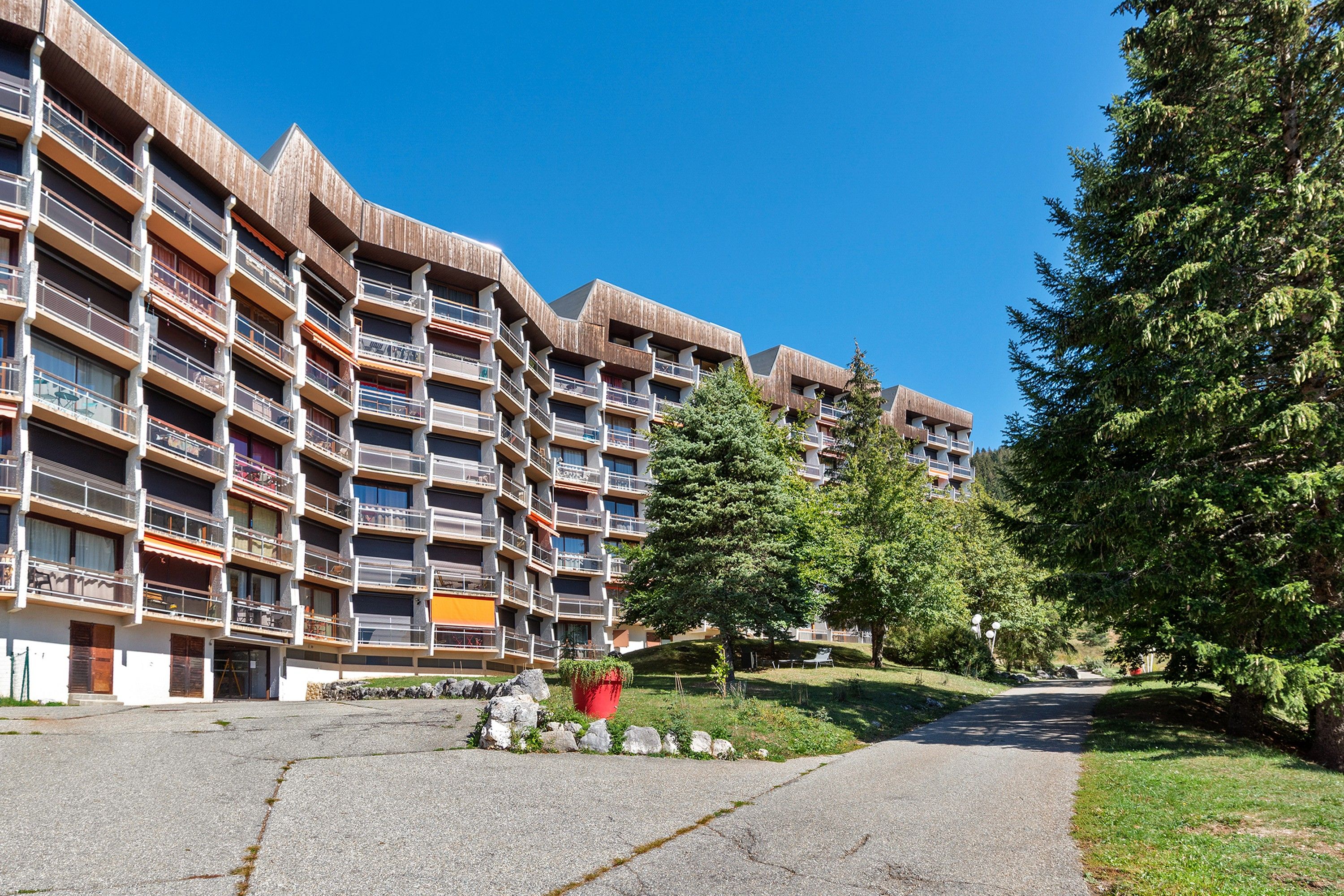 Ein mehrstöckiges Hotel mit Balkonen, einer gepflasterten Auffahrt und umliegender Bepflanzung.