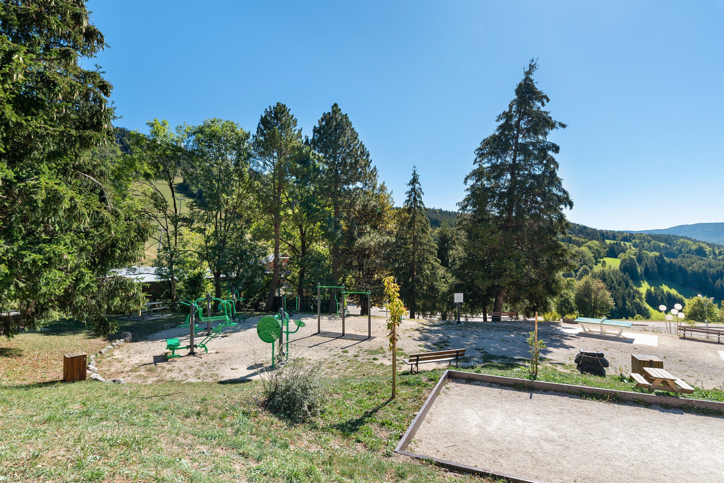 An outdoor park with exercise equipment, benches, and picnic tables.