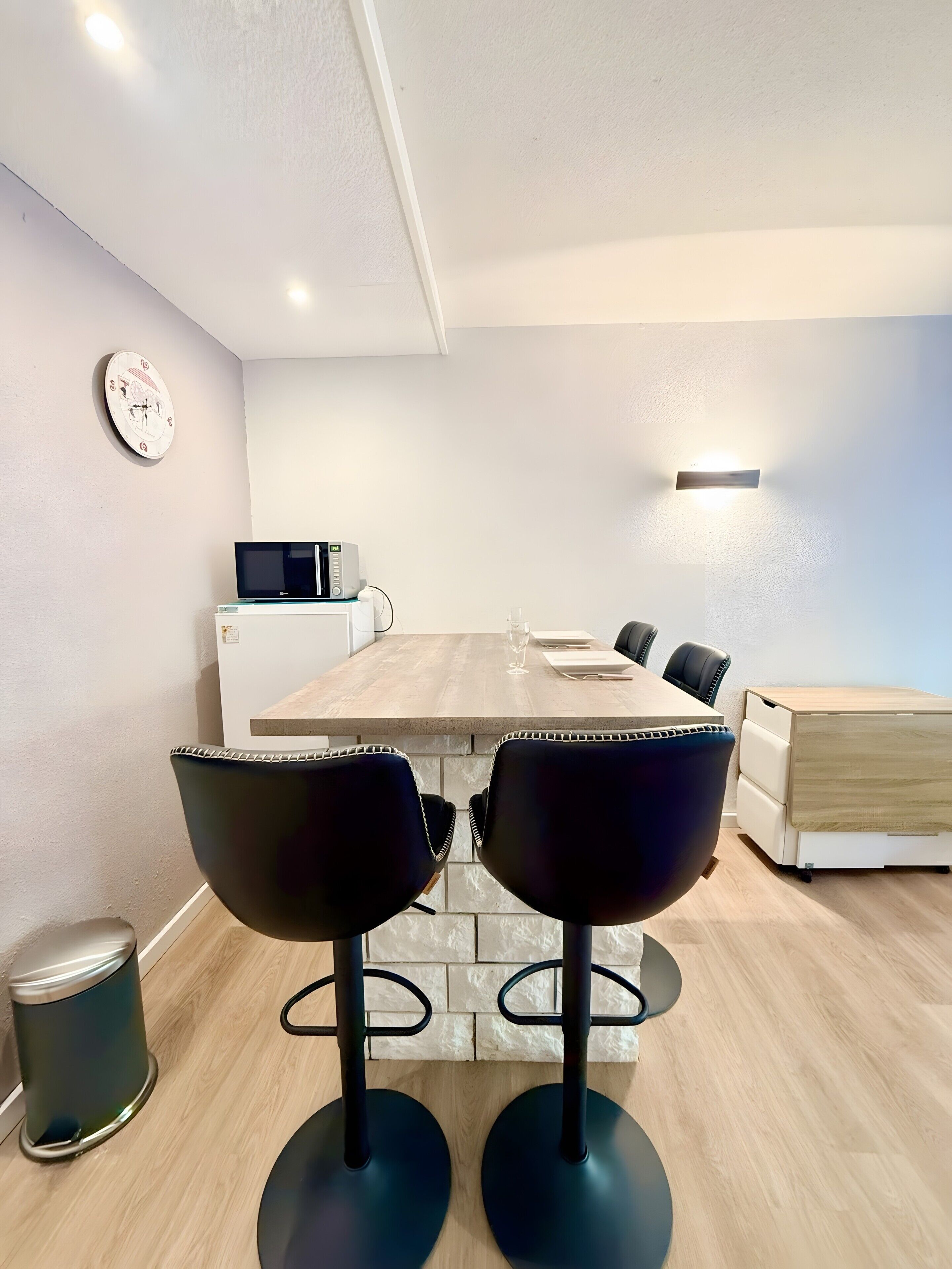 Un comedor moderno con una mesa de madera, dos sillas negras, un reloj y un microondas.