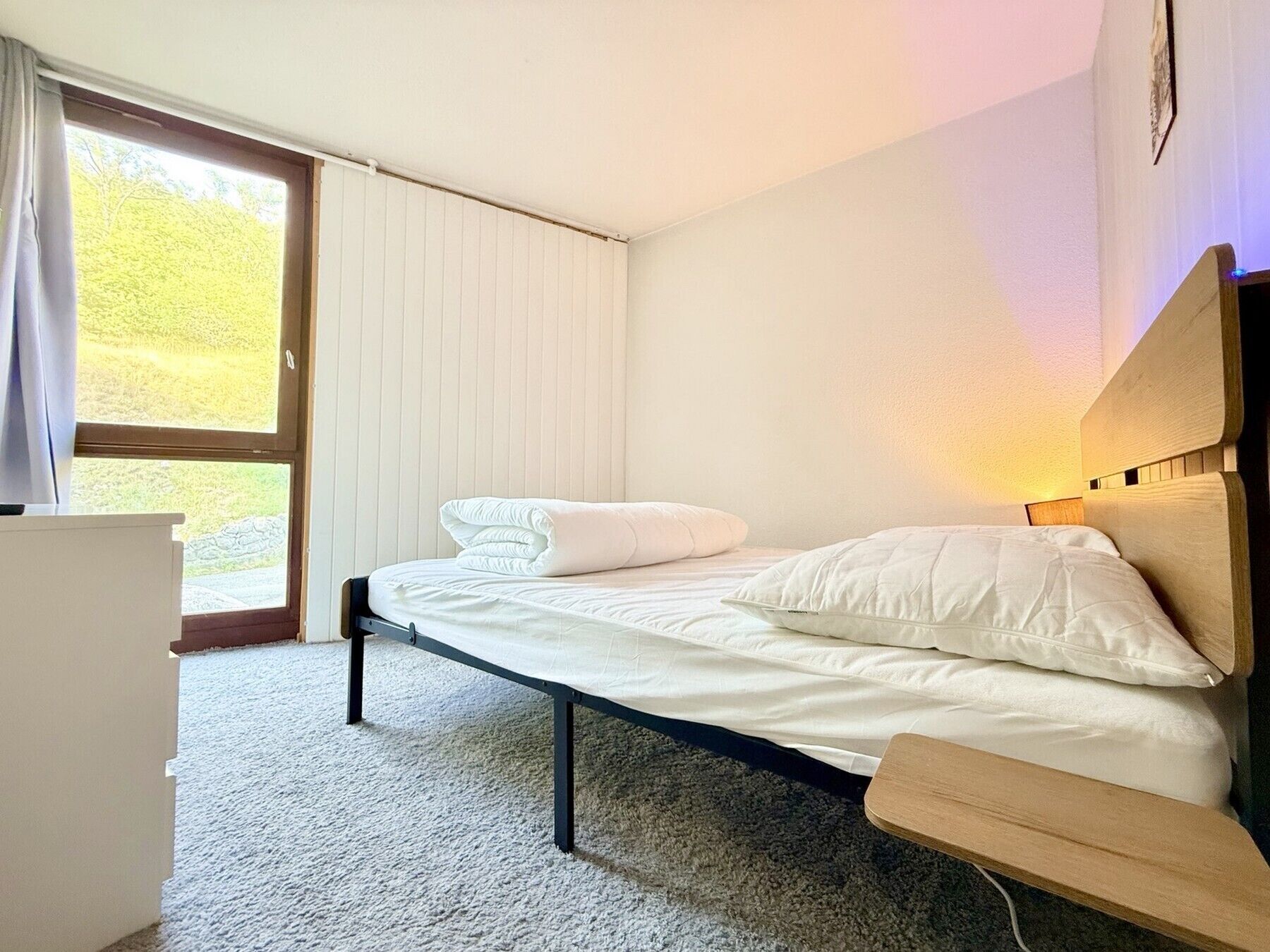 Habitación individual con una cama, cabecera de madera, mesita de noche y ventana con cortinas.