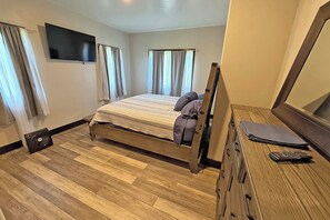 Ein Schlafzimmer mit Bett, Kommode, Fernseher und Vorh ängen.