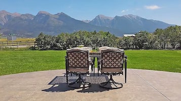 An outdoor patio with two chairs and a table, surrounded by a well-maintained lawn and a view of mountains.
