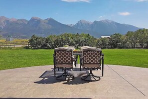 Eine Terrasse im Freien mit zwei Stühlen und einem Tisch, umgeben von einem gepflegten Rasen und Blick auf Berge.