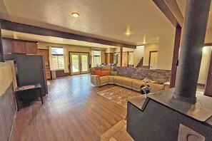 A spacious living area with a large sectional sofa, a fireplace, and a view of the outside through a sliding glass door. - Mission Mountain Escape | Scenic 3BR Retreat (Saint Ignatius)