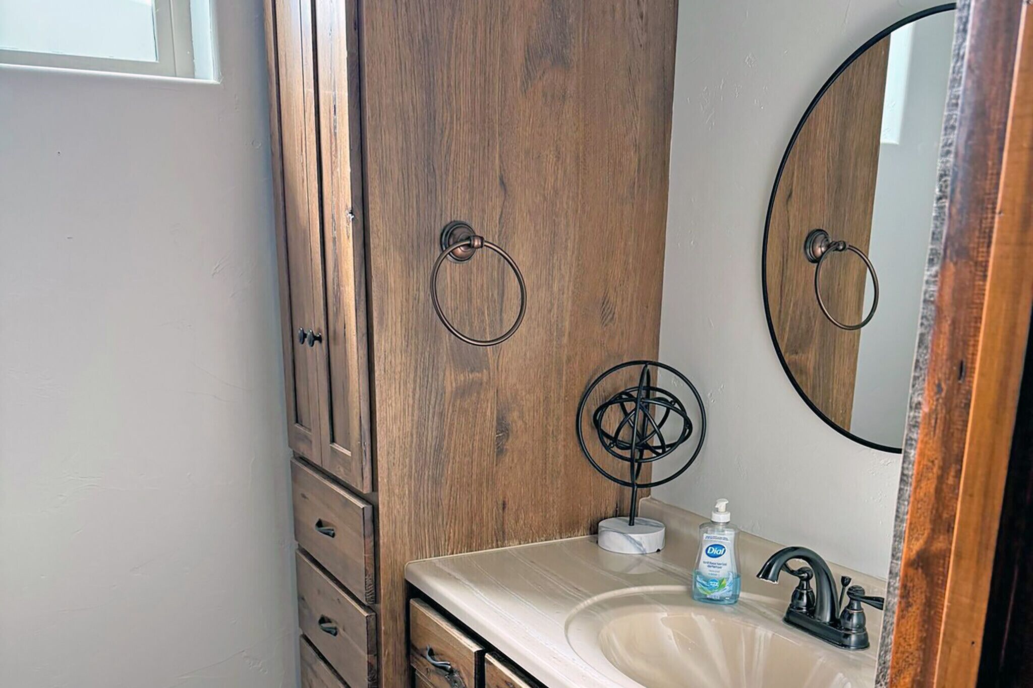 A bathroom with a wooden vanity, a mirror, a sink, and a bottle of hand soap.